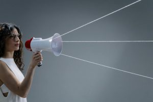 Young woman in a white tank top using a megaphone in a conceptual studio shoot.