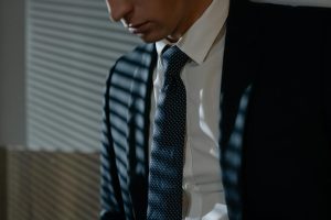 Close-up of a man in a suit and tie under striped shadows, evoking a corporate feel.