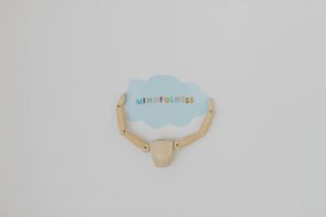 Minimalist image of a wooden figure holding a speech bubble saying 'Mindfulness'.