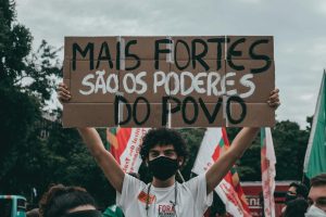 Protester in Rio holds sign saying 'Mais fortes são os poderes do povo.'