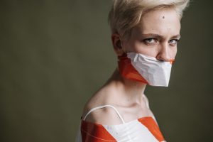 Artistic portrait of a woman with mouth covered by tape, symbolizing silence and oppression.