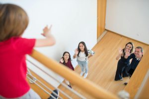 Family waving up at a person in a modern indoor setting, conveying warmth and connection.