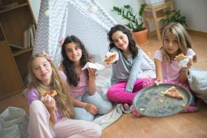 A cheerful group of girls in pajamas enjoying pizza together at an indoor party.