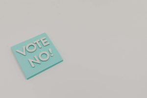 A blue sticky note displaying the message 'Vote No!' on a white surface, minimalistic and impactful.