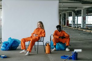 Two workers in orange overalls sit in an industrial warehouse setting, showcasing a modern art portrayal.