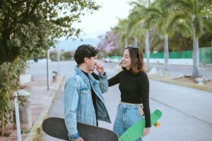 A joyful young couple shares a moment holding skateboards on a sunny street.