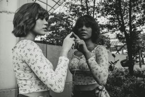 A woman in a monochromatic portrait gazes into a mirror, capturing a reflective moment outdoors.