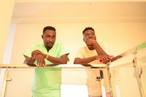 Two men with thoughtful expressions standing by a glass railing indoors in Tema, Ghana.