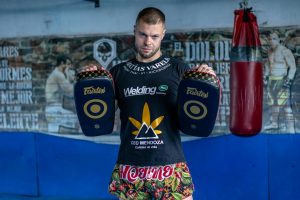 Kickboxer in gym holding training pads, showcasing martial arts attire.