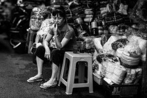 Street vendor sitting among goods in a Hanoi market, Vietnam, showcasing local commerce and lifestyle.