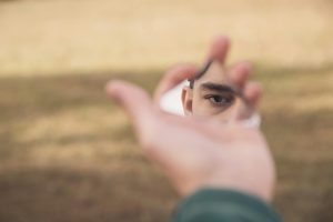 A person's eye reflected in a shard of mirror held outdoors, creating a surreal effect.