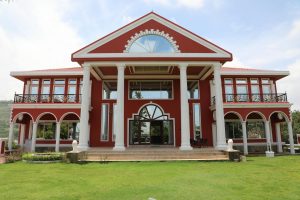 A grand red mansion showcasing classic colonial architecture with lush green surroundings.