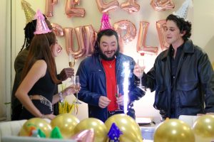 Group of friends celebrating a birthday indoors with cake and champagne.