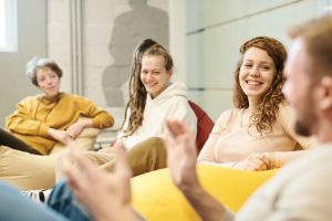 Group of adults enjoying casual conversation indoors on bean bags, sharing happiness and smiles.