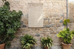 Stone wall with a historic plaque and potted plants in Jaén, Andalucía.