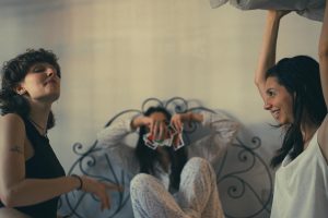 Three women enjoying a playful moment with cards and pillow indoors.