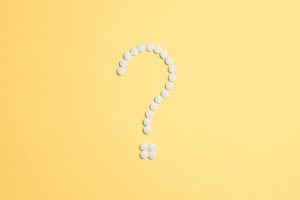 White pills arranged into a question mark shape on a vibrant yellow background.