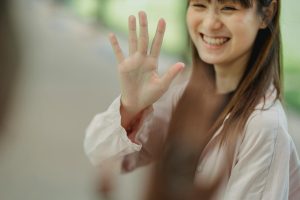 Crop young happy Asian lady saying hi to anonymous partner while looking away on road