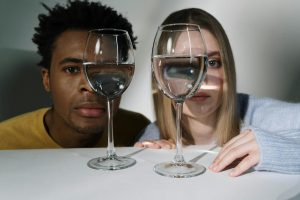 Creative studio shot of a couple peering through wine glasses with distorted reflections.