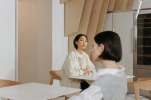 Two women with short hairstyles sitting in a stylish indoor cafe with modern wooden decor.
