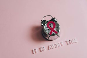 Alarm clock with pink ribbon for breast cancer awareness on pink background.