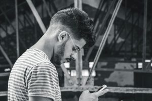 Black-and-white portrait of a man using a smartphone in an industrial location.