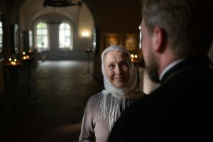 A senior woman and a priest sharing a warm moment in a church interior, with ambient candlelight.