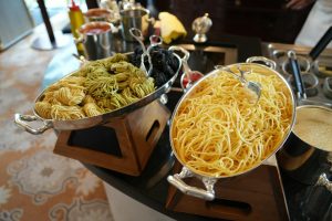 Close-up of assorted pasta varieties displayed in stainless steel trays for a self-serve buffet.