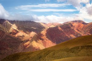 Stunning mountain range under a clear blue sky with clouds, showcasing natural beauty.