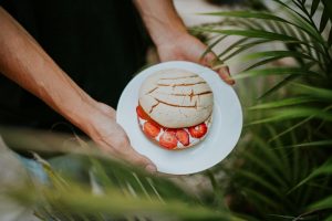 A close-up shot of Mexican pan dulce on a plate, garnished with fresh strawberries, held by hands outdoors.