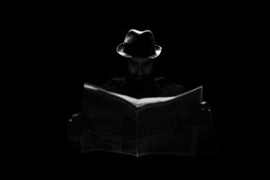 A mysterious figure in a fedora engrossed in reading a newspaper under dramatic lighting.
