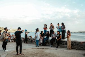 A diverse group of friends relaxing and taking photos by the seaside on a sunny day.