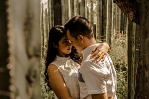 A loving couple embraces face to face in a forest setting, capturing a romantic moment.