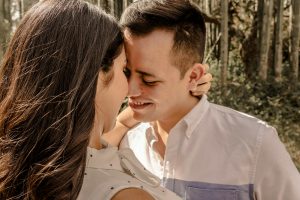 A couple lovingly embracing in a sunlit forest setting, capturing a warm, romantic moment.
