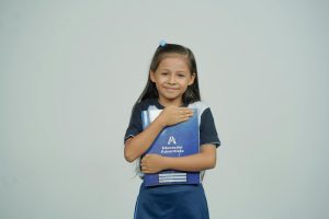 A young girl smiles while holding her school notebook, representing joy in education.