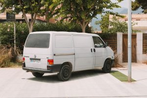 A classic white Volkswagen van parked outdoors in Benidorm, Spain, under the shade of trees.