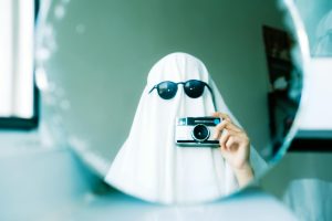 Imaginative Halloween ghost costume using a sheet and sunglasses, holding a camera in front of a mirror.