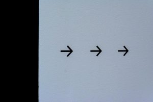 Simple white wall featuring three black arrows pointing right, conveying direction.