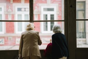 Two elderly women with gray hair look out of a window at a city scene, capturing a serene moment.