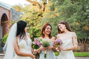 Three bridesmaids holding bouquets, smiling outdoors in a garden setting, Santiago de Querétaro.