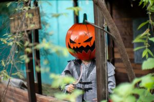 Child wearing a spooky pumpkin head costume in a wooded outdoor Halloween setting in Mexico.