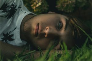 Close-up of a young man lying on grass, gazing thoughtfully. A serene outdoor setting.