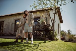 A fashionable couple poses outside a rustic house, embodying modern style.