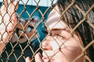 Close-up of a woman looking through a chain link fence capturing natural light.