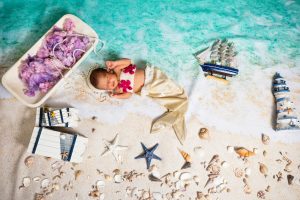 Cute newborn baby dressed as a mermaid in a creative beach-themed setup with seashells and nautical decor.