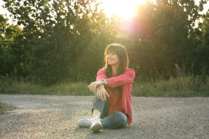 A woman sits on a rural road, enjoying a peaceful summer sunset. Perfect for capturing tranquility.