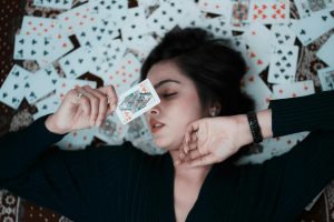 A woman lying on playing cards, holding a card near her face. Creative photoshoot idea.
