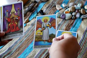 Hands holding tarot cards for a mystical reading on a vibrant cloth with stones.