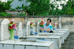A woman cleans gravestones and places colorful flowers in a peaceful cemetery setting.