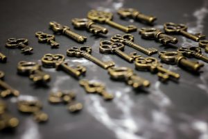 A collection of vintage brass keys displayed in a scattered arrangement on a dark surface.